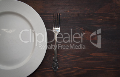 Empty white plate with a fork on a wooden brown surface