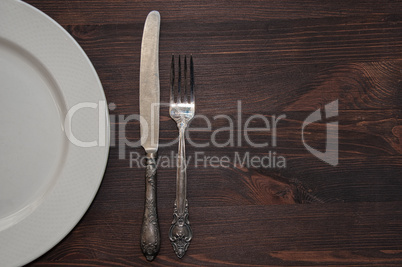 Half of an empty white plate with a fork and a knife on a brown