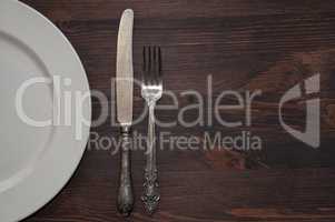 Half of an empty white plate with a fork and a knife on a brown
