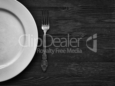 Empty white plate with a fork on a wooden surface, black and whi