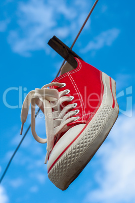 One red sneakers hanging on a clothesline against a blue sky