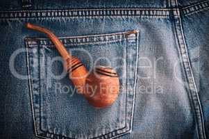 Wooden pipe for tobacco is in the back pocket of old blue jeans