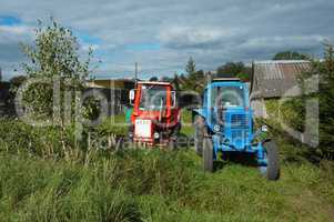 two tractors in a village near the wood house, red and blue tractor are in the yard