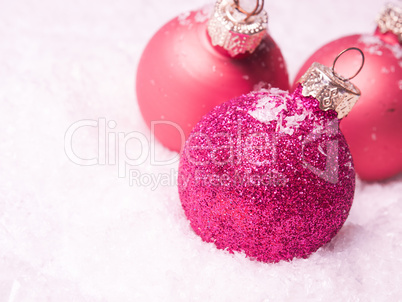 Three pink Christmas baubles in snow