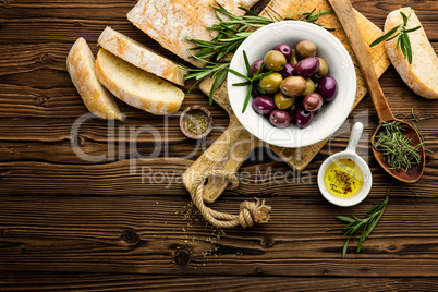 italian food ingredients, rosemary, olives, olive oil and ciabatta bread on wooden background
