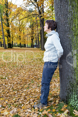 Woman leans in the tree and enjoys the autumn wood