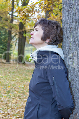 Woman leans in the tree and enjoys the autumn wood