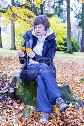 Woman sits in the autumn wood on tree stump