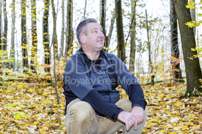 Man sits in the autumn wood on tree stump