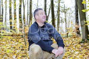 Man sits in the autumn wood on tree stump
