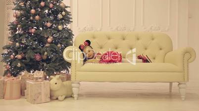 Little cheerful girl sitting on white sofa near the Christmas tree