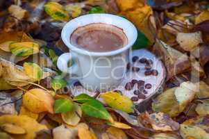 White cup of coffee on a wooden stump among the yellow foliage