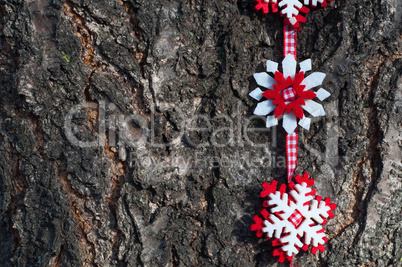 Snowflakes of felt on a red ribbon on a background of tree bark