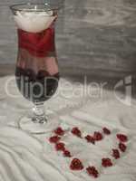 gefülltes Glas im Sand mit Herz aus Rosen
