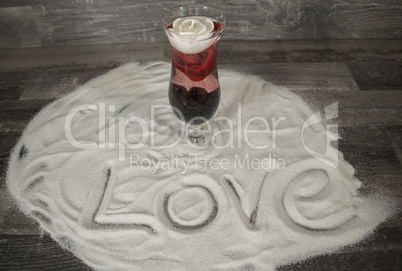 Glas mit Rose und Love Schriftzug im Sand