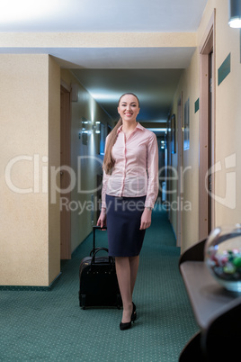 Smiling woman with luggage walks down hallway