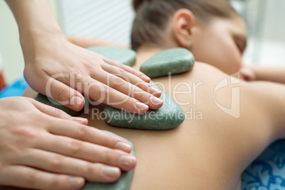 Massage therapist puts spa stones on girl's back