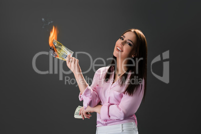 Smiling girl burns money. Concept of extravagance