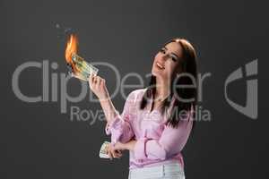 Smiling girl burns money. Concept of extravagance