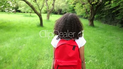 happy mixed race African American girl teenager female young woman hiking with red backpack in green apple orchard