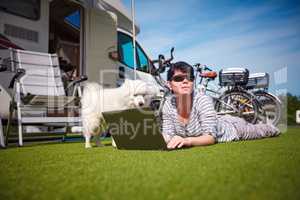 Woman on the grass with a dog looking at a laptop