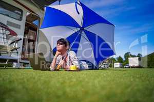 Woman on the grass, looking at the laptop under umbrella near th