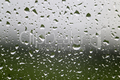 Water raindrop on window glass with green meadow and gray sky