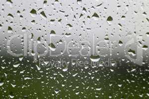 Water raindrop on window glass with green meadow and gray sky