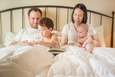 Chinese and Caucasian Baby Boys Reading a Book In Bed with Their