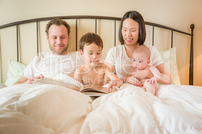 Chinese and Caucasian Baby Boys Reading a Book In Bed with Their