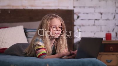 Cute little girl playing with laptop on the bed