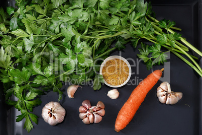 Parsley leaves and vegetables on a dark tray.