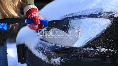 Driver scraping ice from car headlight in winter