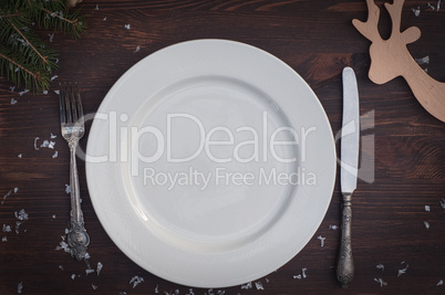 White plate with silver knife and fork on brown wooden surface C