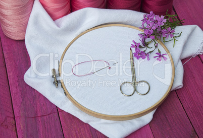 Pink thread and white fabric in the wooden embroidery frame for