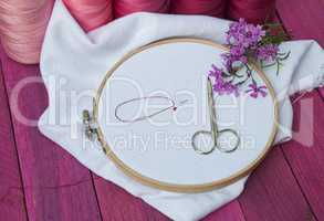 Pink thread and white fabric in the wooden embroidery frame for