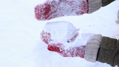 Female hands in knitted mittens making snowball