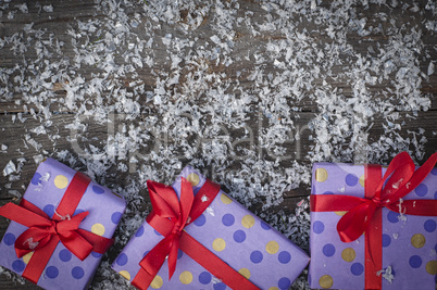 Three gift package with a red ribbon on a wooden surface with sn
