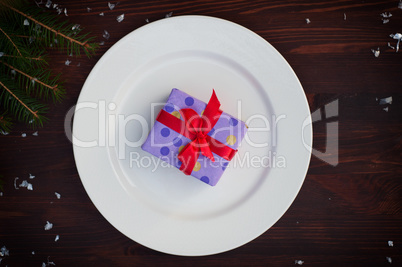 Packed gift with a red ribbon on a white plate