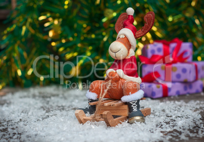 Christmas toy deer in holiday clothes on wooden sleigh among sno