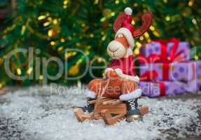Christmas toy deer in holiday clothes on wooden sleigh among sno