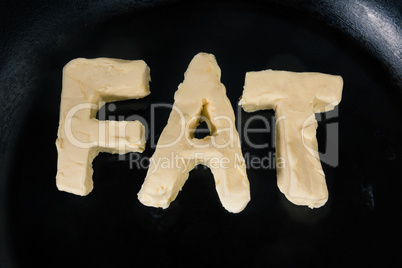 Butter in shape of the word fat on hot pan - Close up top view