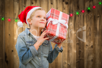 Curious Boy Wearing Santa Hat Holding Christmas Gift On Wood
