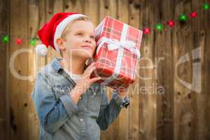 Curious Boy Wearing Santa Hat Holding Christmas Gift On Wood