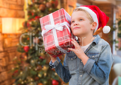 Boy Wearing Santa Hat Holding Christmas Gift In Front of Tree