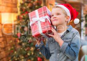 Boy Wearing Santa Hat Holding Christmas Gift In Front of Tree