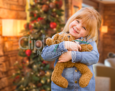 Girl Holding Teddy Bear In Front of Decorated Christmas Tree