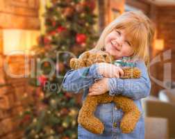 Girl Holding Teddy Bear In Front of Decorated Christmas Tree