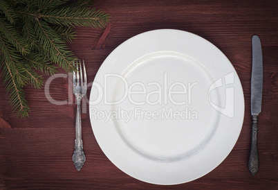 White empty plate with knife and fork on brown wooden surface