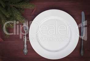 White empty plate with knife and fork on brown wooden surface